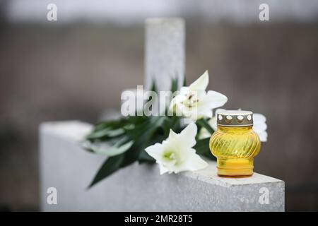 Nénuphars blancs et bougie sur pierre tombale gris clair en plein air. Cérémonie funéraire Banque D'Images