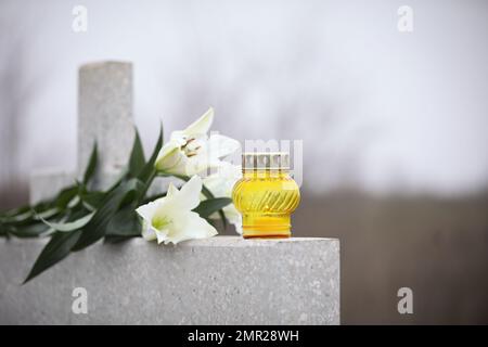 Nénuphars blancs et bougie sur pierre tombale gris clair en plein air. Cérémonie funéraire Banque D'Images