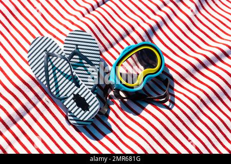 Vue en grand angle des tongs bleues et des articles de natation sur la serviette de plage pendant la journée ensoleillée Banque D'Images