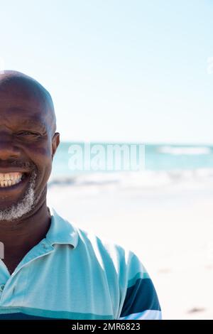 Image rognée d'un homme senior chauve afro-américain souriant, avec vue panoramique sur la mer et le ciel clair Banque D'Images