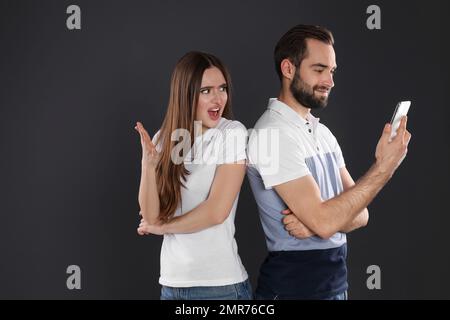 Jeune femme indignée regardant dans le smartphone de l'ami sur fond noir. Problèmes de relation Banque D'Images