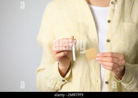 Jeune femme avec timbre de nicotine et cigarette sur fond gris clair, gros plan Banque D'Images