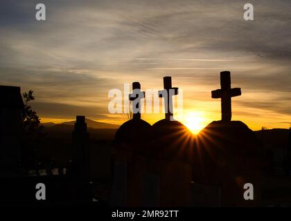 Une belle vue de trois croix dans un jardin avec un ciel orangé de coucher de soleil Banque D'Images