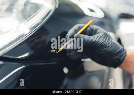 Retouches de peinture de voiture. Mécanicien utilisant une petite brosse pour couvrir les petites rayures sur une voiture noire. Arrière-plan flou. Gros plan. . Photo de haute qualité Banque D'Images