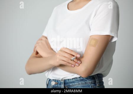 Jeune femme avec timbre de nicotine et cigarette sur fond gris clair, gros plan Banque D'Images