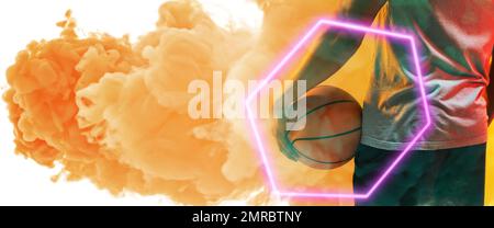 Section médiane d'un joueur de basket-ball biracial tenant le ballon avec un hexagone sur fond fumé Banque D'Images