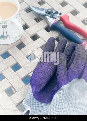 Un coup de tête de gants de jardinage et de sécateurs sur une table extérieure - pause thé après le travail de jardin Banque D'Images