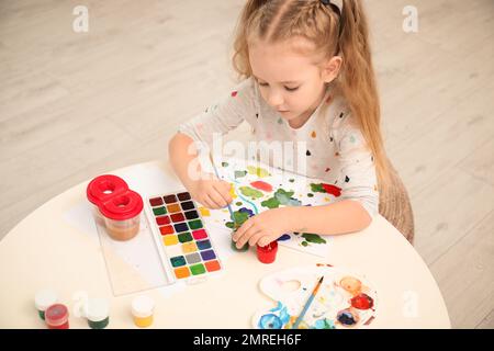 Joli petit enfant peint à la table dans la chambre Banque D'Images