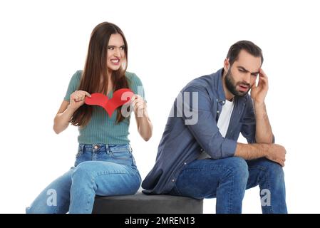 Femme déchirant le coeur de papier près de son petit ami sur fond blanc. Problèmes de relation Banque D'Images