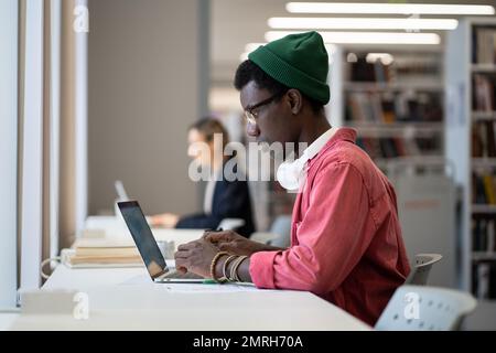 Un homme afro-américain indépendant et entrepreneur est assis avec un ordinateur portable dans un bâtiment de bibliothèque Banque D'Images