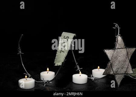 Numéro de prisonnier, badge juif, barbelés et bougies allumées sur fond noir. Journée internationale de commémoration de l'Holocauste Banque D'Images