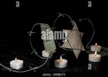 Numéro de prisonnier, badge juif, barbelés et bougies allumées sur fond noir. Journée internationale de commémoration de l'Holocauste Banque D'Images