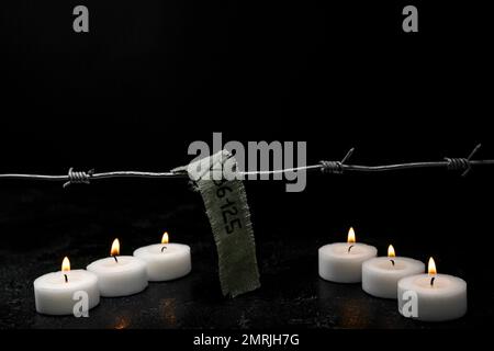 Numéro de prisonnier, barbelés et bougies allumées sur fond sombre. Journée internationale de commémoration de l'Holocauste Banque D'Images