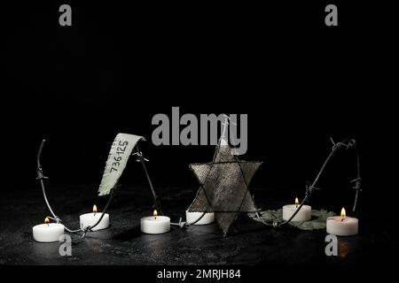 Numéro de prisonnier, badge juif, barbelés et bougies allumées sur fond noir avec espace pour le texte. Journée internationale de commémoration de l'Holocauste Banque D'Images