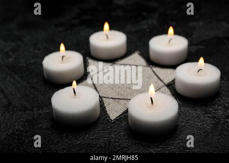 Bougies allumées et badge juif sur fond sombre. Journée internationale de commémoration de l'Holocauste Banque D'Images