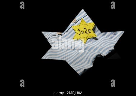 Uniforme de prisonnier et badge juif visibles à travers la forme de l'étoile David sur fond noir avec espace pour le texte. Journée internationale de commémoration de l'Holocauste Banque D'Images
