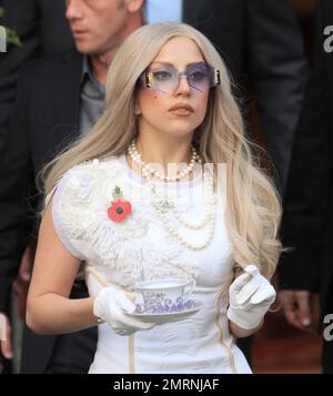Megastar Lady Gaga, qui ressemble à une dame, quitte son hôtel londonien dans une robe à motifs blancs, un collier de perles, des lunettes de soleil hexagonales et assorties avec des gants blancs tout en tenant un thé et une soucoupe. Gaga montre du respect le dimanche du souvenir en portant un coquelicot sur sa poitrine. L'homme de 25 ans devrait prendre le pas sur les résultats en direct du « facteur X » d'aujourd'hui. Londres, Royaume-Uni. 13th novembre 2011. . Banque D'Images