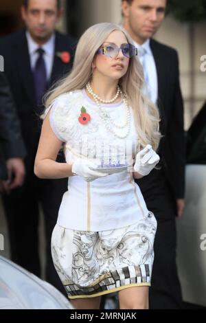 Megastar Lady Gaga, qui ressemble à une dame, quitte son hôtel londonien dans une robe à motifs blancs, un collier de perles, des lunettes de soleil hexagonales et assorties avec des gants blancs tout en tenant un thé et une soucoupe. Gaga montre du respect le dimanche du souvenir en portant un coquelicot sur sa poitrine. L'homme de 25 ans devrait prendre le pas sur les résultats en direct du « facteur X » d'aujourd'hui. Londres, Royaume-Uni. 13th novembre 2011. . Banque D'Images