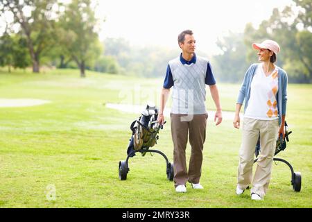 Couple se préparer à jouer au golf. Pleine longueur d'un couple attrayant marchant avec des sacs de golf. Banque D'Images