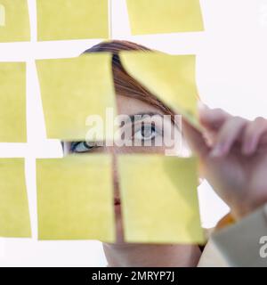 Visualisez, élaborez des stratégies, concrétisez. une femme d'affaires qui organise des notes adhésives sur un wal en verre. Banque D'Images