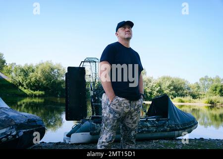 portrait d'un homme en vacances dans la nature, à bord d'un hydroglisseur sur la rivière en vêtements de chasseur Banque D'Images