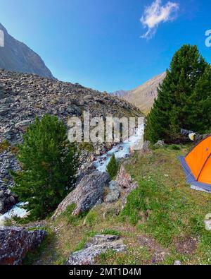 Le bord d'une tente orange touristique près d'une falaise avec une rivière dans les montagnes de l'Altaï. Banque D'Images