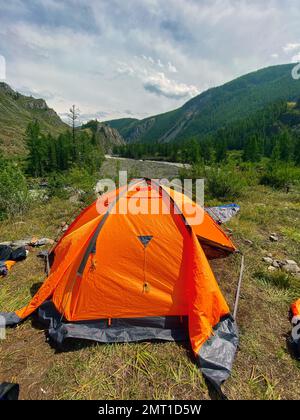 Une tente touristique orange est ouverte pendant la journée près d'une falaise dans une gorge des montagnes de l'Altaï Banque D'Images