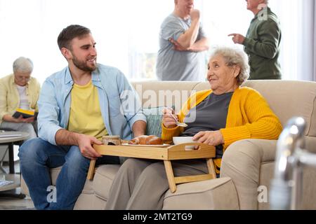 Jeune homme servant un dîner pour une femme âgée dans un hospice gériatrique. Soins aux personnes âgées Banque D'Images