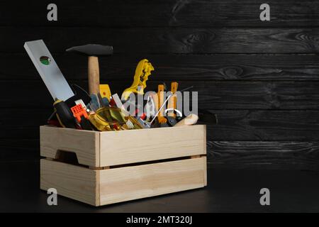 Caisse en bois avec différents outils de menuisier sur table noire. Espace pour le texte Banque D'Images