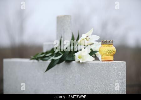 Nénuphars blancs et bougie sur pierre tombale gris clair en plein air. Cérémonie funéraire Banque D'Images