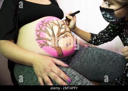 Séance de peinture corporelle sur le ventre d'une femme enceinte de huit mois. Dessin d'un arbre Banque D'Images