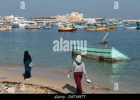 Alexandrie, Égypte. 1 décembre 2022 deux musulmanes marchent sur la plage près d'un bateau en contrebas devant la citadelle de Qaitrava, la ville d'Alexandrie, Banque D'Images