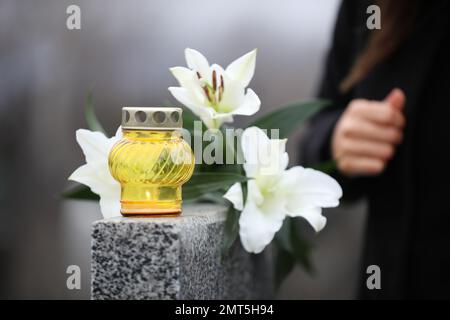 Femme près de pierre tombale de granit gris avec des fleurs à l'extérieur, foyer sur bougie. Cérémonie funéraire Banque D'Images