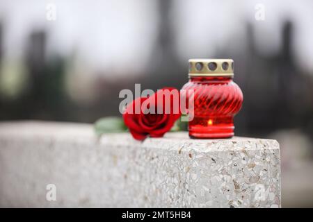 Rose rouge et bougie sur pierre tombale gris clair en plein air. Cérémonie funéraire Banque D'Images