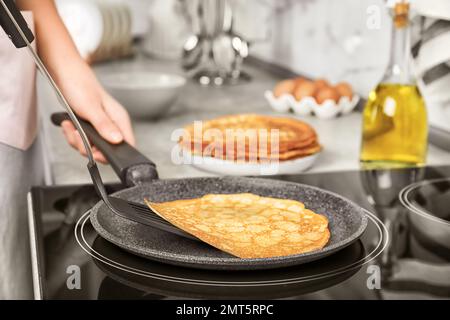 Femme cuisant de délicieuses crêpes fines sur cuisinière à induction, gros plan Banque D'Images