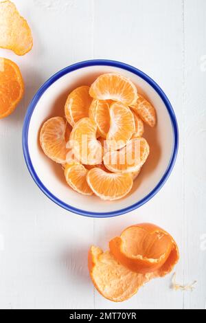 Tranches de mandarine pelée dans un bol, vue de dessus. Gros plan d'un orange mandarin sur fond blanc. Banque D'Images