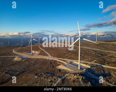 Moulins à vent sur les collines pendant le coucher du soleil. Énergies renouvelables, énergies vertes. Montagnes en arrière-plan avec de la neige. Énergie éolienne et écologique. Banque D'Images