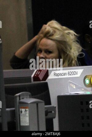 Pamela Anderson garde au chaud dans une robe pull en laine marron et des bottes hauteur genou associées à une écharpe blanche floue lorsqu'elle arrive à LAX. Anderson était tout sourire à son arrivée et a traversé le point de contrôle de sécurité de la TSA avant de prendre son vol. Los Angeles, Californie. 12/7/10. Banque D'Images