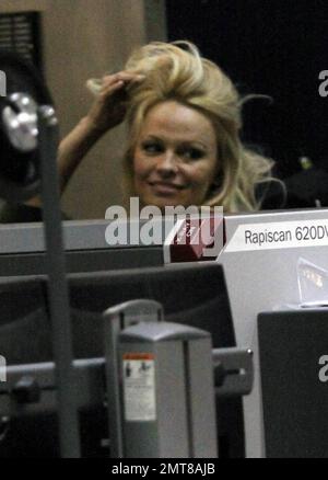 Pamela Anderson garde au chaud dans une robe pull en laine marron et des bottes hauteur genou associées à une écharpe blanche floue lorsqu'elle arrive à LAX. Anderson était tout sourire à son arrivée et a traversé le point de contrôle de sécurité de la TSA avant de prendre son vol. Los Angeles, Californie. 12/7/10. Banque D'Images