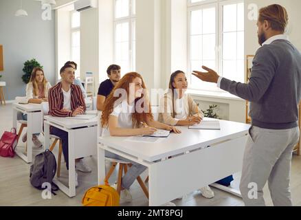 Les élèves du secondaire écoutent attentivement un professeur barbu. Intérieur moderne de la salle de classe. Banque D'Images
