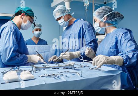 Groupe de chirurgiens concentrés pendant l'opération chirurgicale en salle d'opération, vue latérale. Travail d'équipe en service chirurgical Banque D'Images