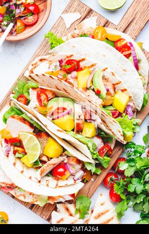 Tacos au poulet grillé, sauce à la sauce tomate, mangue, coriandre et oignon dans la tortilla sur la planche à découper. Arrière-plan de table blanc, vue du dessus Banque D'Images