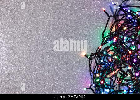 Guirlande électrique d'ampoules colorées sur fond argenté avec paillettes. Vue de dessus, espace de copie Banque D'Images