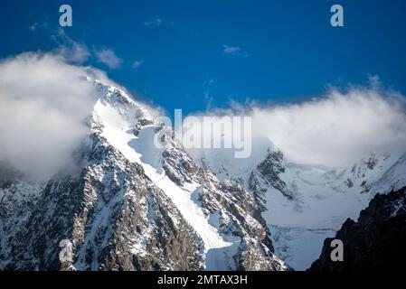 Les sommets des montagnes de pierre rocheuse avec des langues de glaciers et de neige sont couverts de nuages blancs et de brouillard en Altaï pendant la journée. Banque D'Images