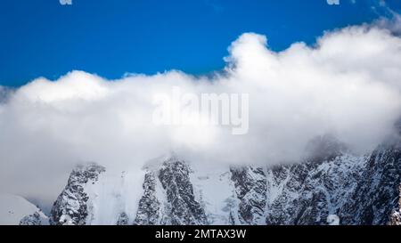 Les sommets des montagnes rocheuses avec des langues de glaciers et de neige sont couverts de nuages blancs et de brouillard en Altaï pendant la journée. Banque D'Images