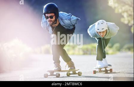 Sports, vitesse et sécurité, patinage en bord de mer sur route, amis qui font de la descente avec skateboard et casque. Aventure sportive extrême, skate Street Banque D'Images