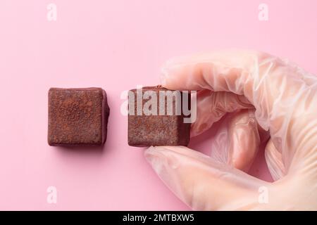 Bonbon au chocolat peint fait à la main dans une main humaine. Délicieux dessert sur fond rose avec espace publicitaire Banque D'Images
