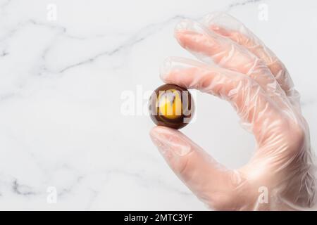 Bonbon au chocolat peint fait à la main dans une main humaine. Délicieux dessert sur fond blanc avec espace publicitaire Banque D'Images