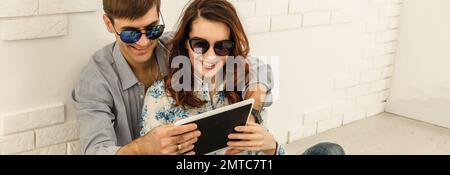 Couple heureux avec tablette, shopping en ligne, faire des commandes sur Internet assis à la maison dans le salon vide Banque D'Images