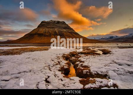 Une vue panoramique d'une colline rocheuse au coucher du soleil avec de la neige à son pied Banque D'Images